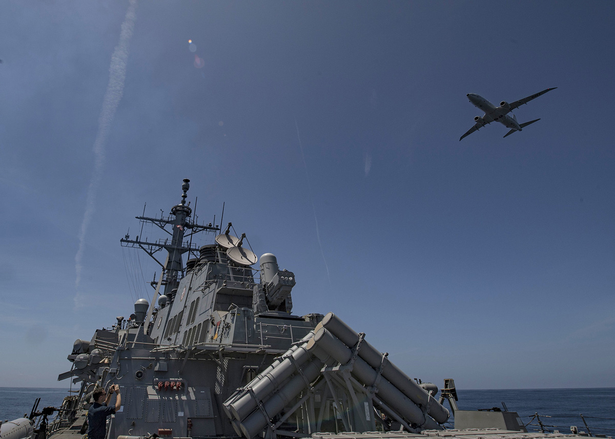 A P-8 Poseidon flies over the Arleigh Burke-class guided-missile destroyer USS Carney (DDG 64) during a air defense exercise, June 19, 2019.
